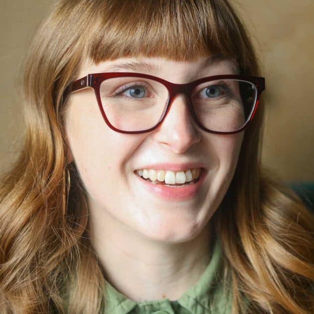 Woman wearing blue light blocking glasses in a red cat eye shape.